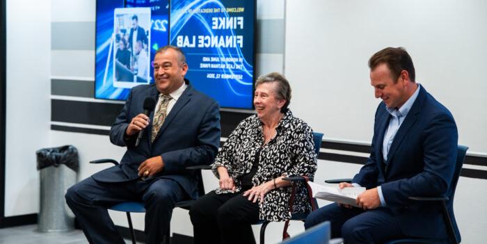 Three panelists sit at the front of the room in raised chairs. The panelists smile at the audience.